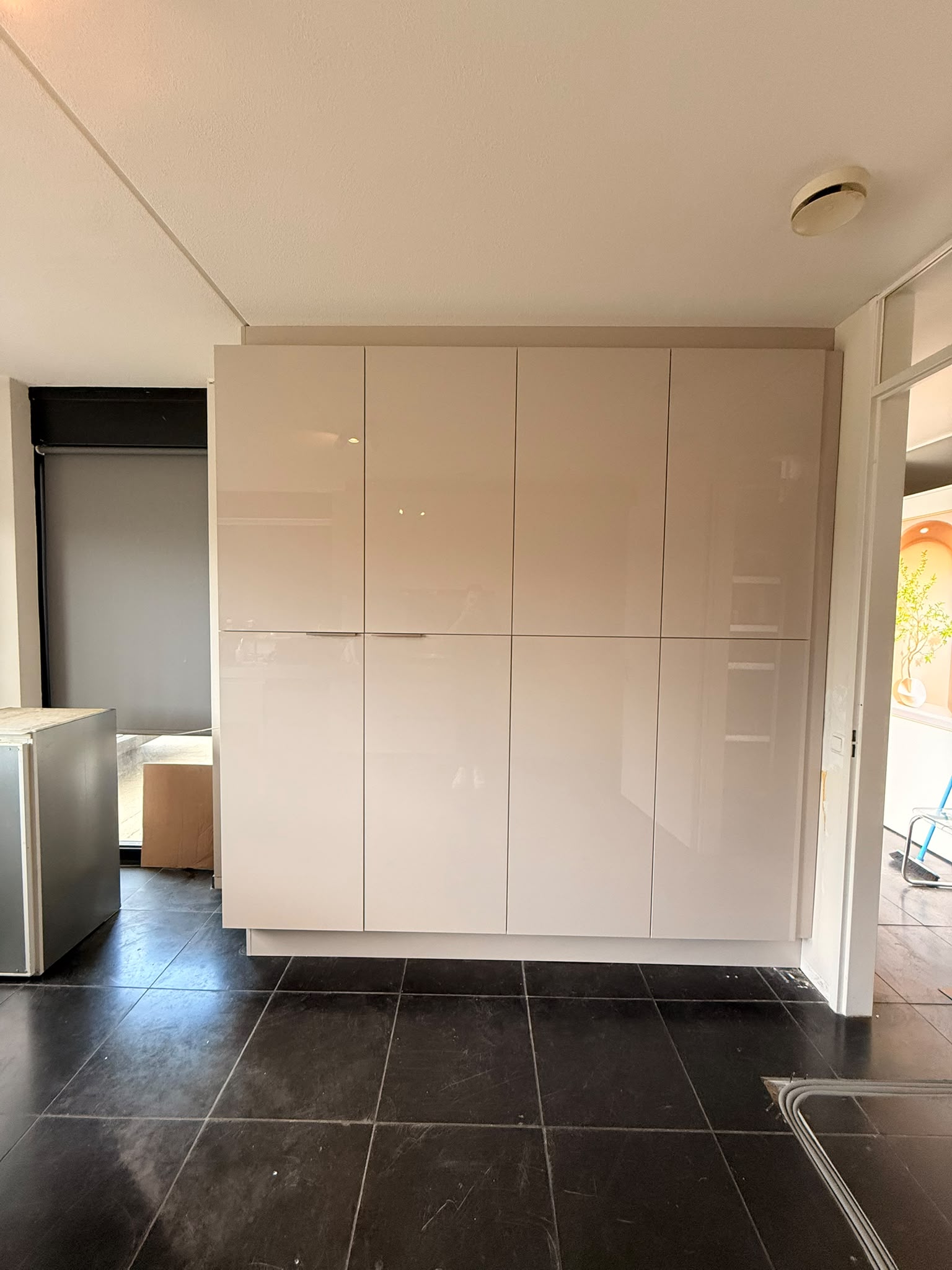 Wand met nieuwe hoge opbergkasten in lichte hoogglans, deuren dicht