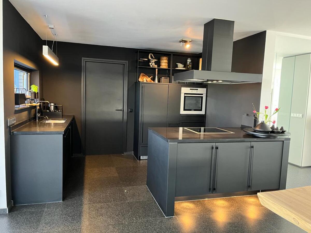 Mat zwarte industriële keuken met kookeiland en houtlook-accenten
